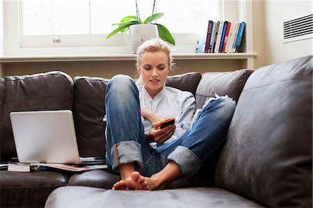 Young woman sitting on sofa and looking at smartphone Stock Photo - Premium Royalty-Free, Code: 614-06442466