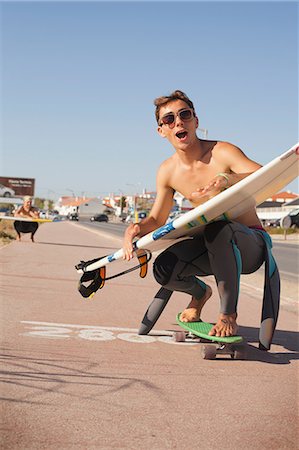 Young man skateboarding down street whilst holding a surfboard Stock Photo - Premium Royalty-Free, Code: 614-06442470