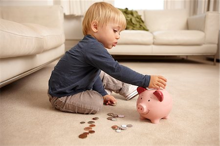 Boy putting coins in piggy bank Stock Photo - Premium Royalty-Free, Code: 614-06443000