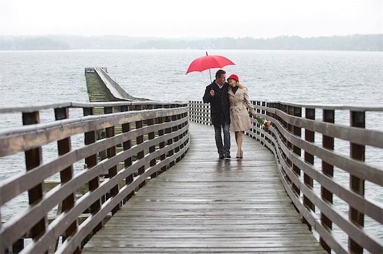 Couple walking on wooden pier in rain Stock Photo - Premium Royalty-Free, Image code: 614-06536902