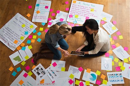 Colleagues sitting on floor with digital tablet, papers and adhesive notes Stock Photo - Premium Royalty-Free, Code: 614-06718141