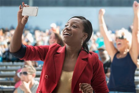 excited african american sport - Woman in stadium, recording event with her phone Stock Photo - Premium Royalty-Free, Code: 614-06718197