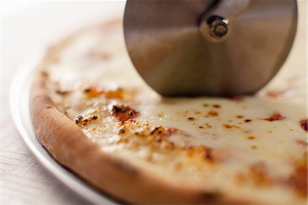 fresh cheese - Close up of cutter slicing pizza Photographie de stock - Premium Libres de Droits, Code: 614-06720034