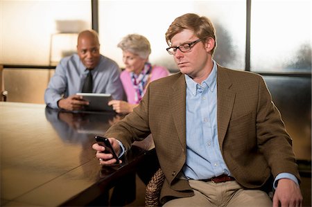 simsearch:614-06814076,k - Young man using cell phone with colleagues in background Stock Photo - Premium Royalty-Free, Code: 614-06814057
