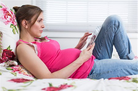 Pregnant woman lying on bed looking at digital tablet Fotografie stock - Premium Royalty-Free, Codice: 614-06813756