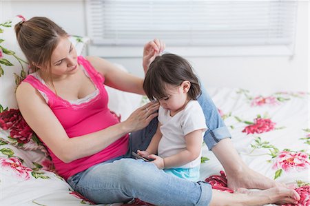 Pregnant woman and toddler daughter on bed looking at smartphone Stock Photo - Premium Royalty-Free, Code: 614-06813757