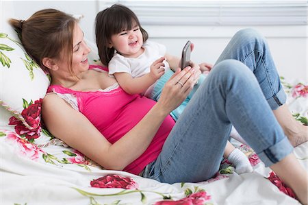 expectativa - Portrait of pregnant woman and toddler daughter lounging on bed playing with smartphone Foto de stock - Sin royalties Premium, Código: 614-06813761