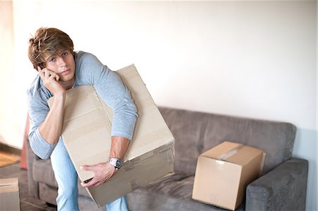 Young man moving house on cell phone carrying box Stock Photo - Premium Royalty-Free, Code: 614-06813781