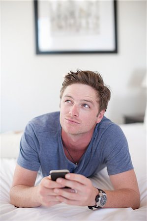 Young man holding smartphone, looking away Stock Photo - Premium Royalty-Free, Code: 614-06813944