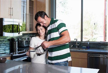 Young couple pouring coffee from pot in kitchen, smiling Stock Photo - Premium Royalty-Free, Code: 614-06895878