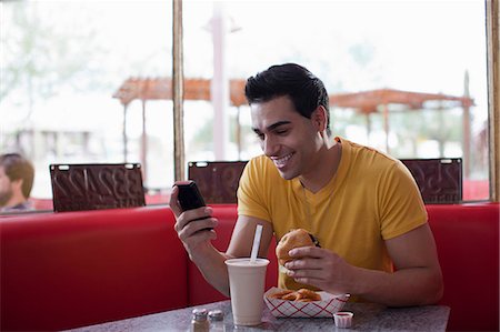 Young man texting on mobile phone and eating fast food in diner Stock Photo - Premium Royalty-Free, Code: 614-06896137