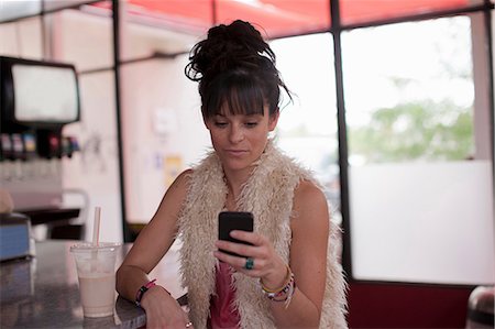 person with milkshake - Young woman looking at mobile phone in diner Stock Photo - Premium Royalty-Free, Code: 614-06896143