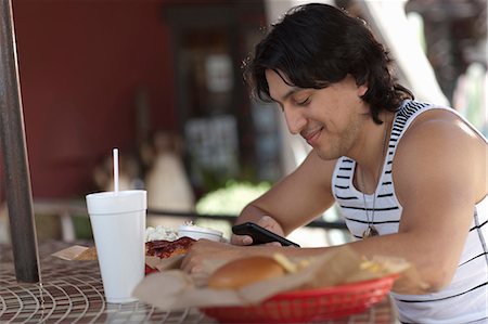 fast food - Young man looking at mobile phone in outdoor cafe, smiling Stock Photo - Premium Royalty-Free, Code: 614-06896223