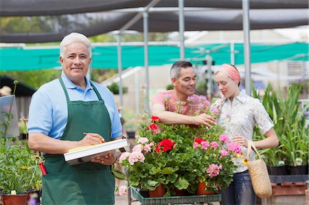 simsearch:614-06896287,k - Senior gardener using clipboard with customers in background of garden centre Stock Photo - Premium Royalty-Free, Code: 614-06896301