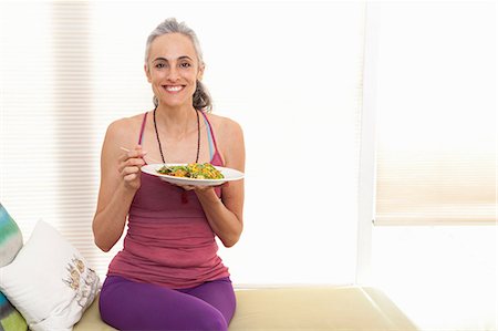 Woman sitting on window seat eating lunch, portrait Stock Photo - Premium Royalty-Free, Code: 614-06896672