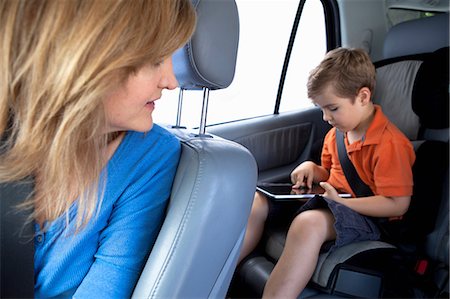 Mother watching son use digital tablet in back seat of car Stock Photo - Premium Royalty-Free, Code: 614-06896690