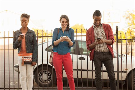 phone african american adults - Three friends using cell phones by metal fence Stock Photo - Premium Royalty-Free, Code: 614-06896792