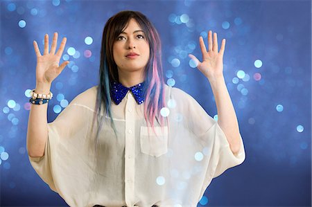 Portrait of young woman with arms up looking at glitter Stock Photo - Premium Royalty-Free, Code: 614-06896872