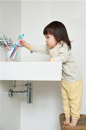 Girl toddler on tiptoe reaching over bathroom sink Stock Photo - Premium Royalty-Free, Code: 614-06896917