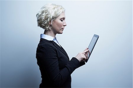 Studio portrait of blond businesswoman looking at digital tablet Foto de stock - Sin royalties Premium, Código: 614-06897242