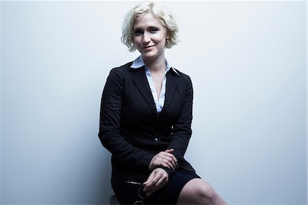 Studio portrait of blond businesswoman sitting on stool Stock Photo - Premium Royalty-Free, Code: 614-06897243