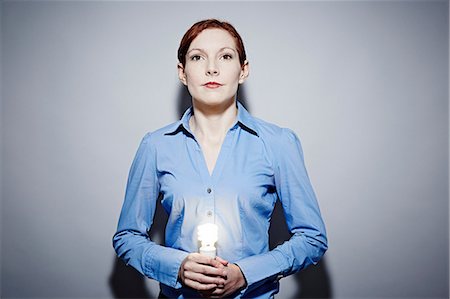 Studio portrait of young business woman holding lit lightbulb Stock Photo - Premium Royalty-Free, Code: 614-06897265