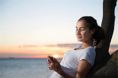 earplug - Close up of young woman leaning on tree at dusk Stock Photo - Premium Royalty-Free, Code: 614-06897285