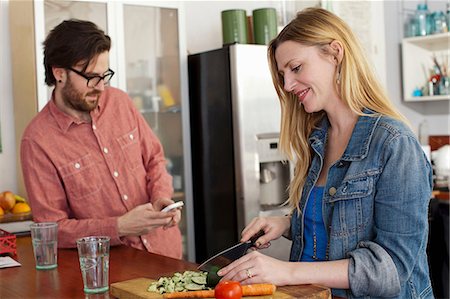 Woman chopping vegetables, man using smartphone Stock Photo - Premium Royalty-Free, Code: 614-06897567