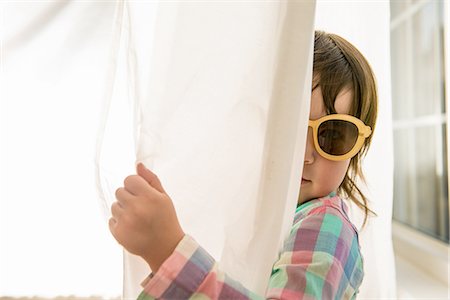 Girl peering round curtain wearing sunglasses Stock Photo - Premium Royalty-Free, Code: 614-06897709
