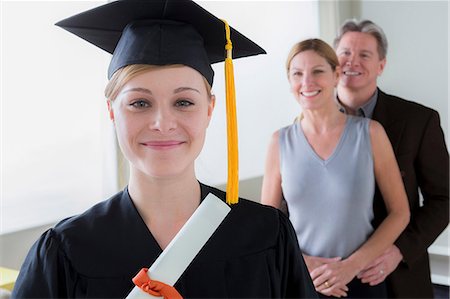 Teenage girl wearing mortarboard with parents in background Stock Photo - Premium Royalty-Free, Code: 614-06897832