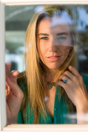 regarder par la fenêtre - Portrait of young woman looking through window, hand in hair Photographie de stock - Premium Libres de Droits, Code: 614-06897927