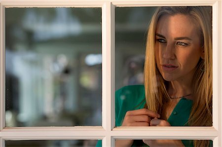 Portrait of young woman looking through window Stock Photo - Premium Royalty-Free, Code: 614-06897928