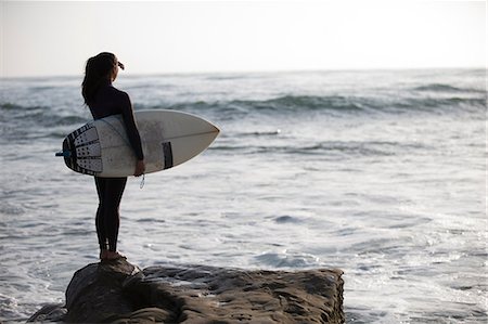 roupa molhada - Young woman standing on rocks with surfboard Foto de stock - Royalty Free Premium, Número: 614-06897950