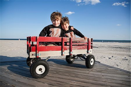 red white - Two brothers in cart on beach with arms around each other Stock Photo - Premium Royalty-Free, Code: 614-06897998