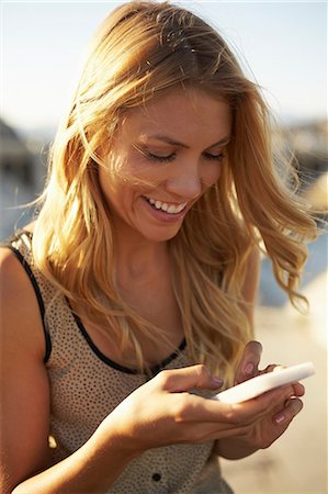 Woman smiling at text message on mobile phone Stock Photo - Premium Royalty-Free, Code: 614-06898347