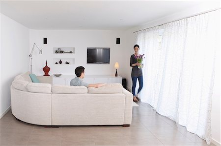 people sitting on a sofa - Man looking at woman walking away with vase of flowers Stock Photo - Premium Royalty-Free, Code: 614-06898605