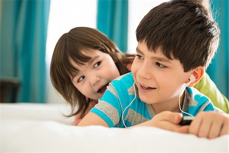 Girl looking at boy listening to mp3 player on bed Stock Photo - Premium Royalty-Free, Code: 614-06974051