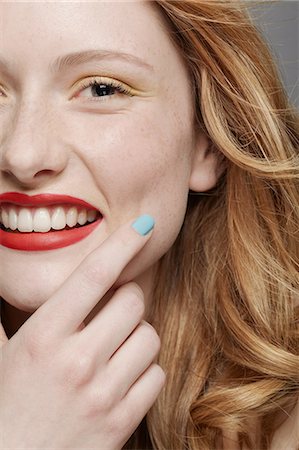 Studio shot of young woman with curly red hair wearing make up, hand on chin Stock Photo - Premium Royalty-Free, Code: 614-06974536