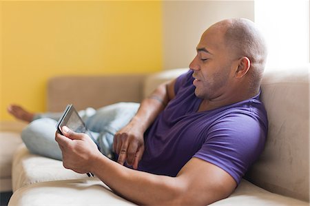 purple people - Mid adult male on sofa with digital tablet Stock Photo - Premium Royalty-Free, Code: 614-06974765