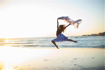 energetic person jumping - Young woman dancing on sunlit beach Stock Photo - Premium Royalty-Free, Code: 614-06973610