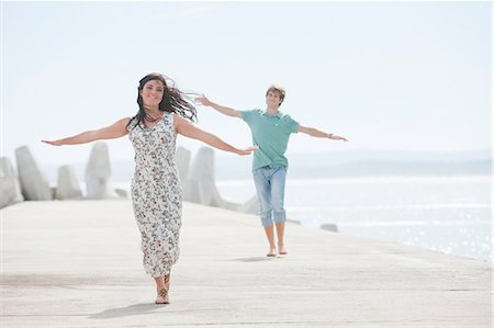 freeing (to set free) - Happy young couple with arms outstretched on pier Stock Photo - Premium Royalty-Free, Code: 614-06973737