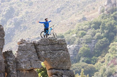 distance (émotion) - Young man with mountain bike and arms outstretched on rock Photographie de stock - Premium Libres de Droits, Code: 614-06973758