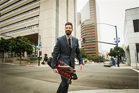 funky - Young businessman carrying skateboard and crossing street Stock Photo - Premium Royalty-Free, Code: 614-07031174