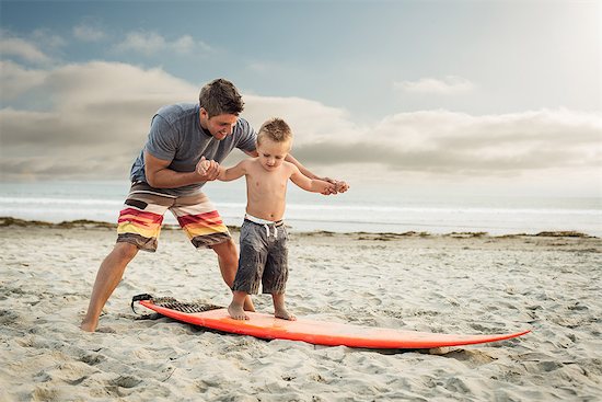 Young man teaching son to surf on beach Photographie de stock - Premium Libres de Droits, Le code de l’image : 614-07031194