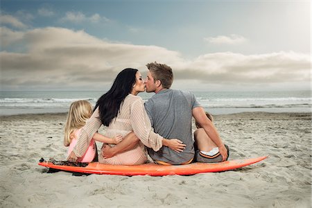 father and kid at the beach - Young family sitting on surfboard on beach with parents kissing Stock Photo - Premium Royalty-Free, Code: 614-07031191