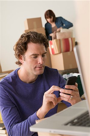 rodeado - Man texting on cellphone whilst moving house Foto de stock - Sin royalties Premium, Código: 614-07031325