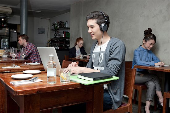 Young man wearing headphones using laptop in cafe Stock Photo - Premium Royalty-Free, Image code: 614-07031545