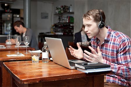 skype - Young man wearing headphones using laptop in cafe Foto de stock - Sin royalties Premium, Código: 614-07031543