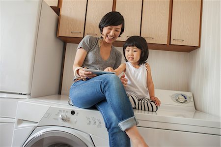 screen time - Mother and daughter sitting on washing machine using tablet Photographie de stock - Premium Libres de Droits, Code: 614-07031658