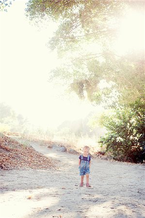 Young female toddler with hands in pockets on dirt track Stock Photo - Premium Royalty-Free, Code: 614-07031821